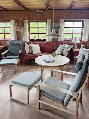 A cozy room with wooden walls, a round table, and seating arrangements including a sofa and chairs. - Thatched holiday home on the Limfjord's edge (Spoettrup)