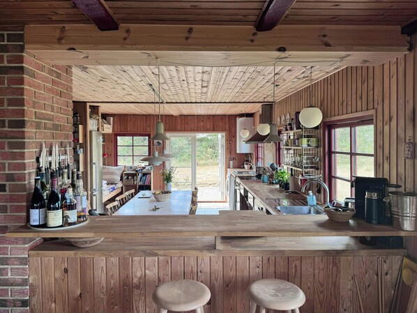 A rustic kitchen with wooden beams, a central island with stools, and a brick wall. - Thatched holiday home on the Limfjord's edge (Spoettrup)