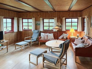 Ein gemütliches Zimmer mit Holzwänden, einem Ledersofa, einem Holztisch und einem Fernseher auf einem Holzständer.