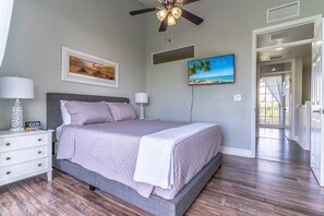 A bedroom with a bed, nightstands, a ceiling fan, and artwork on the walls.