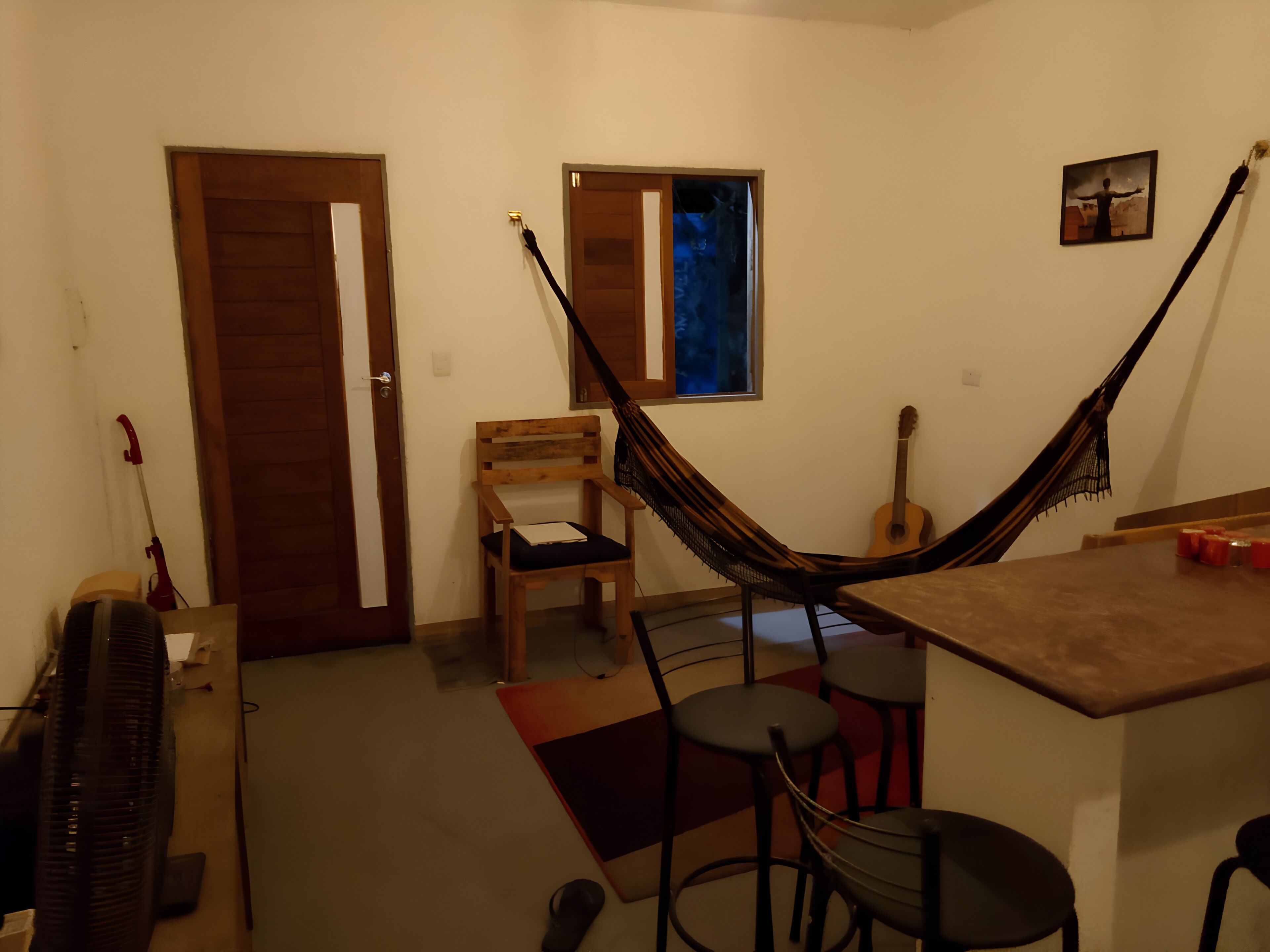 A room with a hammock, a guitar, a chair, and a table.