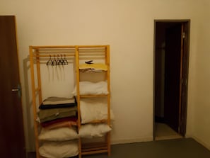 A room with a wooden wardrobe containing folded clothes and a hanging rack with clothes.