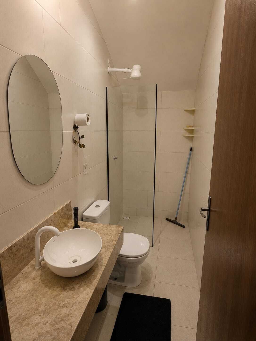 A modern bathroom with a round mirror, a sink, a toilet, and a shower area.
