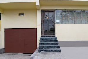 Un edificio con una puerta marrón, un conjunto de escalones que llevan a una entrada con reja y un ventanal con detalles decorativos.