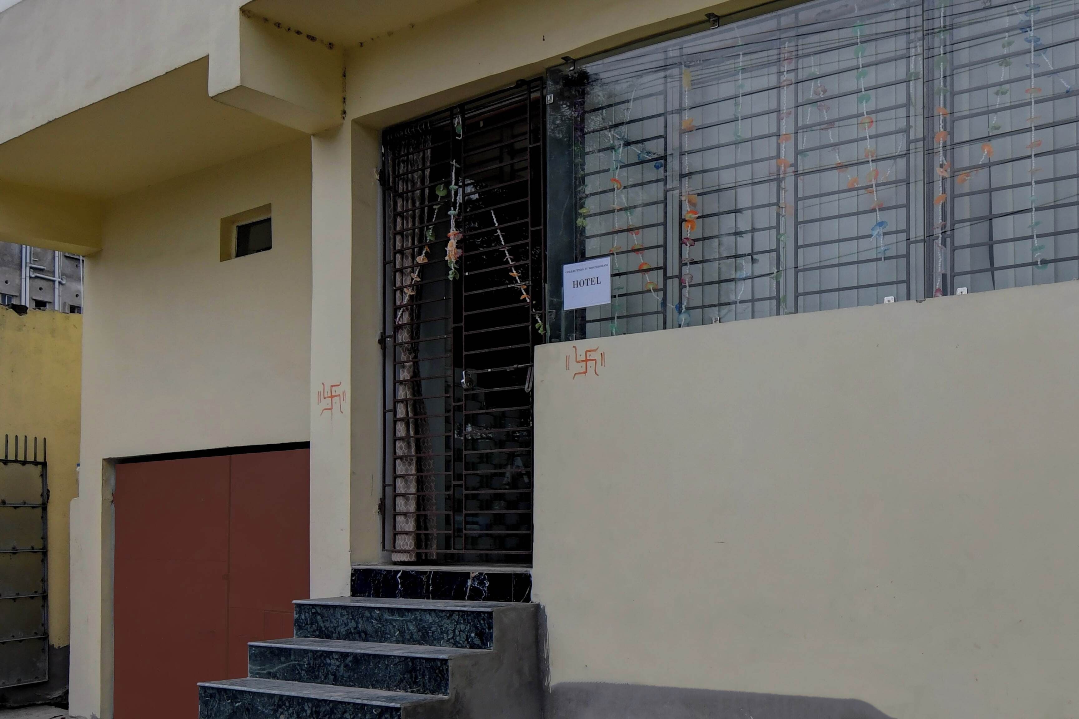 Entrada de hotel con una reja metálica, una escalera que lleva a la puerta y un cartel con el nombre del hotel.