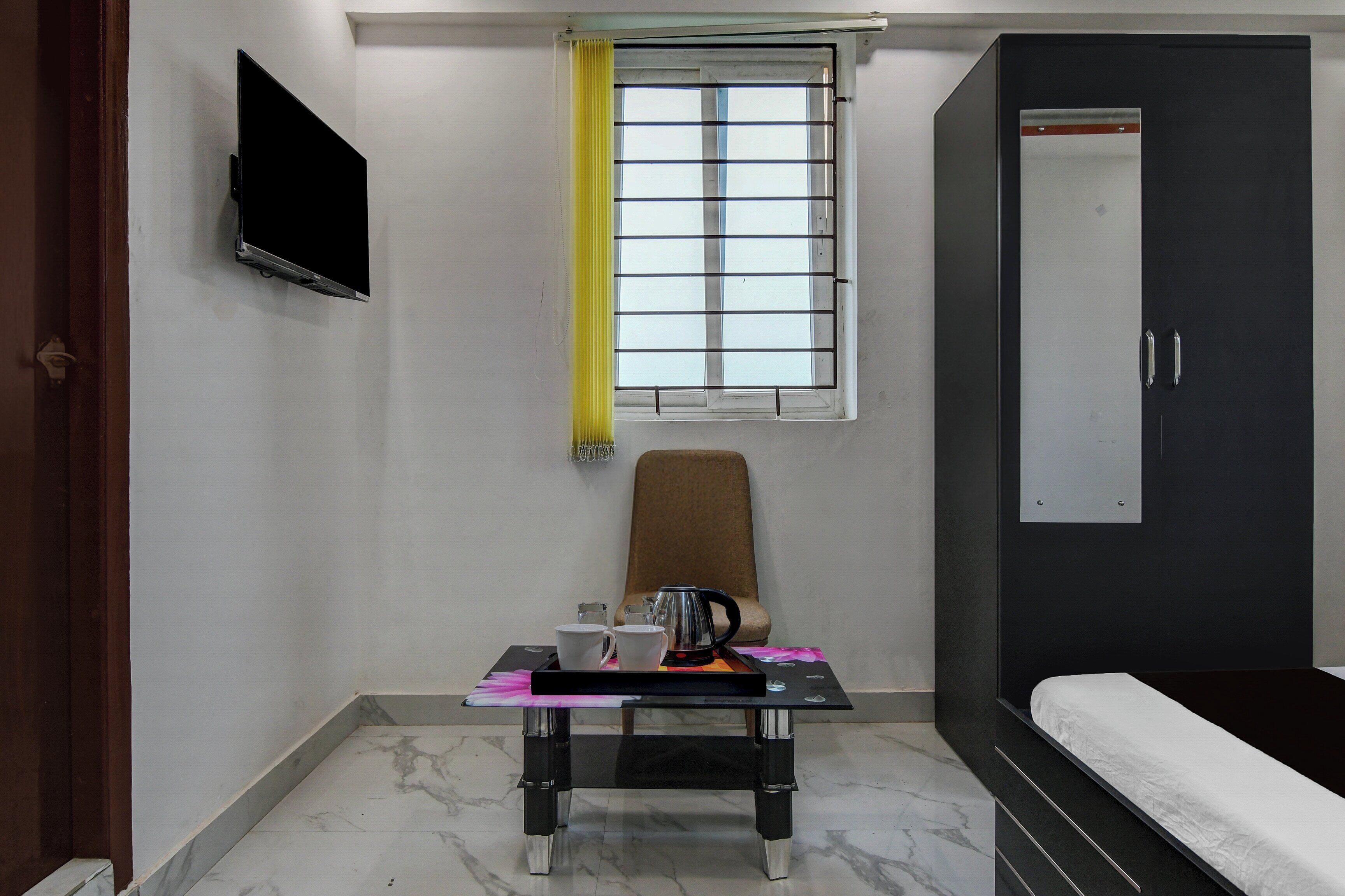 A small, compact room with a bed, a desk with a chair, a television mounted on the wall, and a window with a curtain.