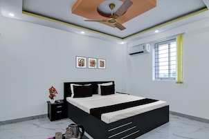 Un dormitorio moderno con cama, mesitas de noche, ventilador de techo, equipo de aire acondicionado y ventana con vistas.