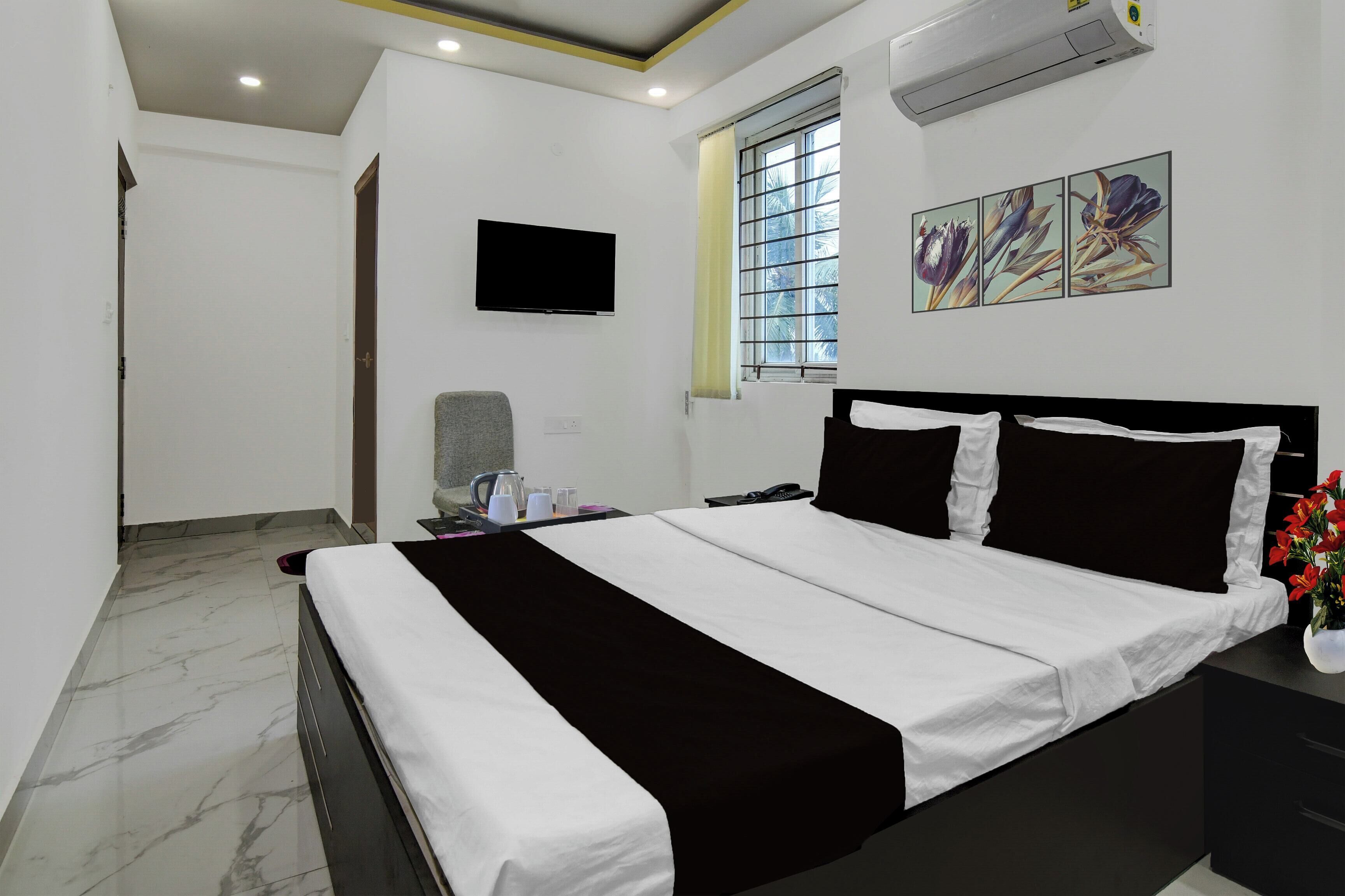 Habitación de hotel con cama, televisor de pantalla plana, ventana con vista a palmeras y aire acondicionado montado en la pared.