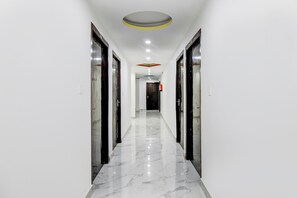 Un pasillo de paredes blancas y suelo de mármol, que conduce a una habitación con una puerta al final.