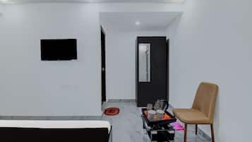 A hotel room with a bed, a chair, a small table with a kettle, and a TV mounted on the wall.