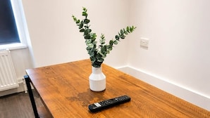 Una mesa de comedor de madera con un control remoto y una planta en maceta.