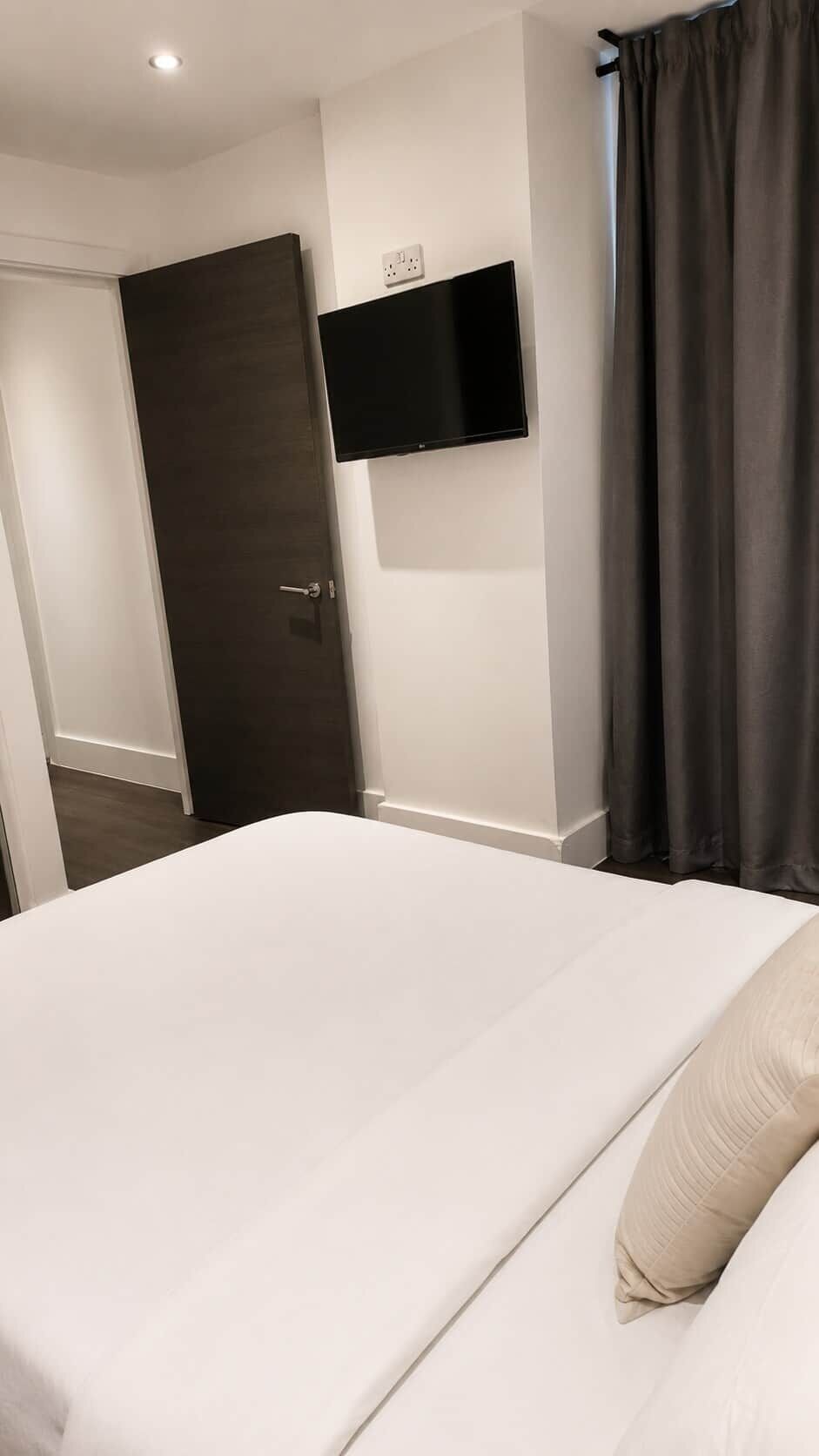 Habitación de hotel con cama, televisor de pantalla plana en la pared, una puerta y una cortina.