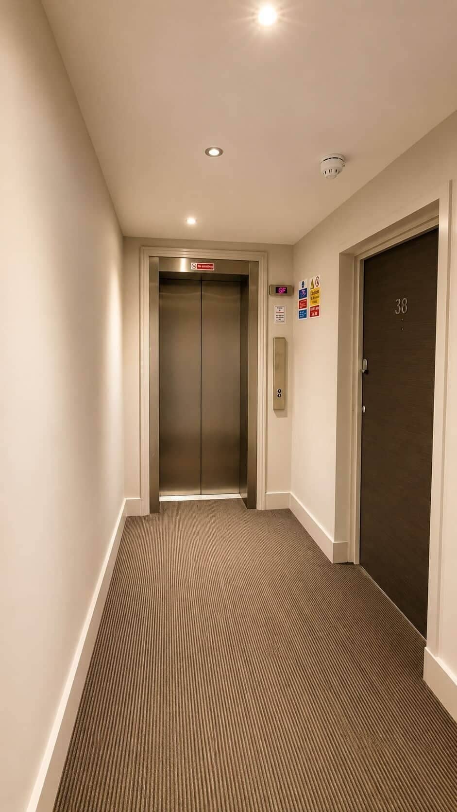 A hallway with an elevator, a door marked with the number 38, and a fire alarm on the wall.