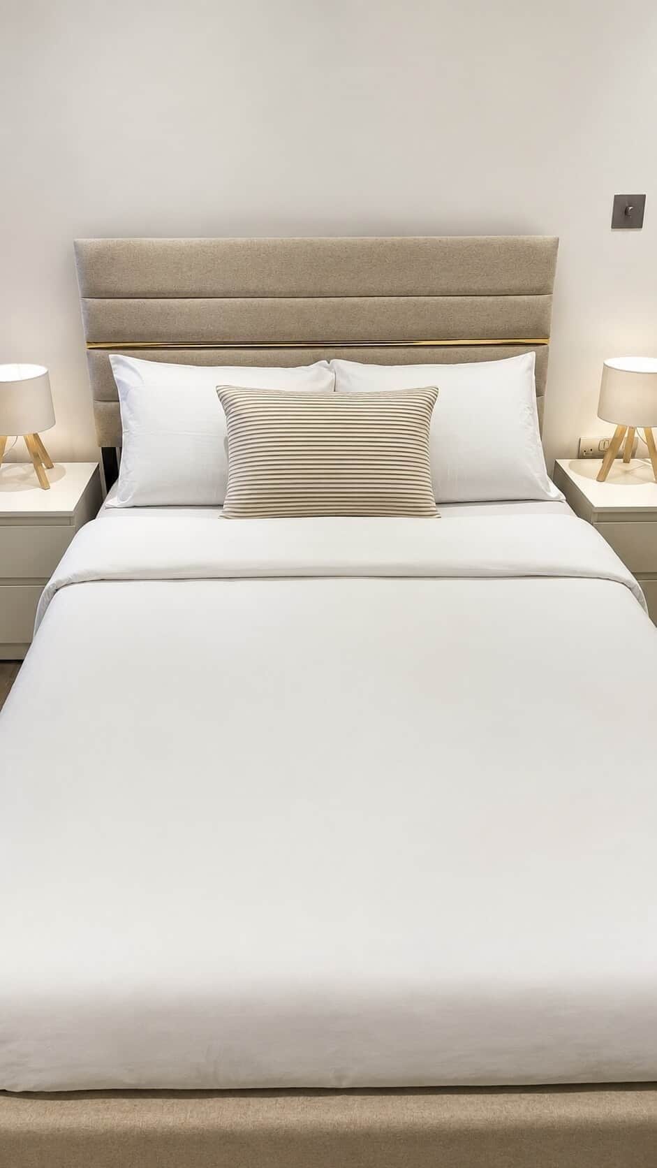 A neatly made bed with a headboard, two bedside tables with lamps, and a wall-mounted light switch.