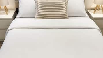 A neatly made bed with a headboard, two bedside tables with lamps, and a wall-mounted light switch.