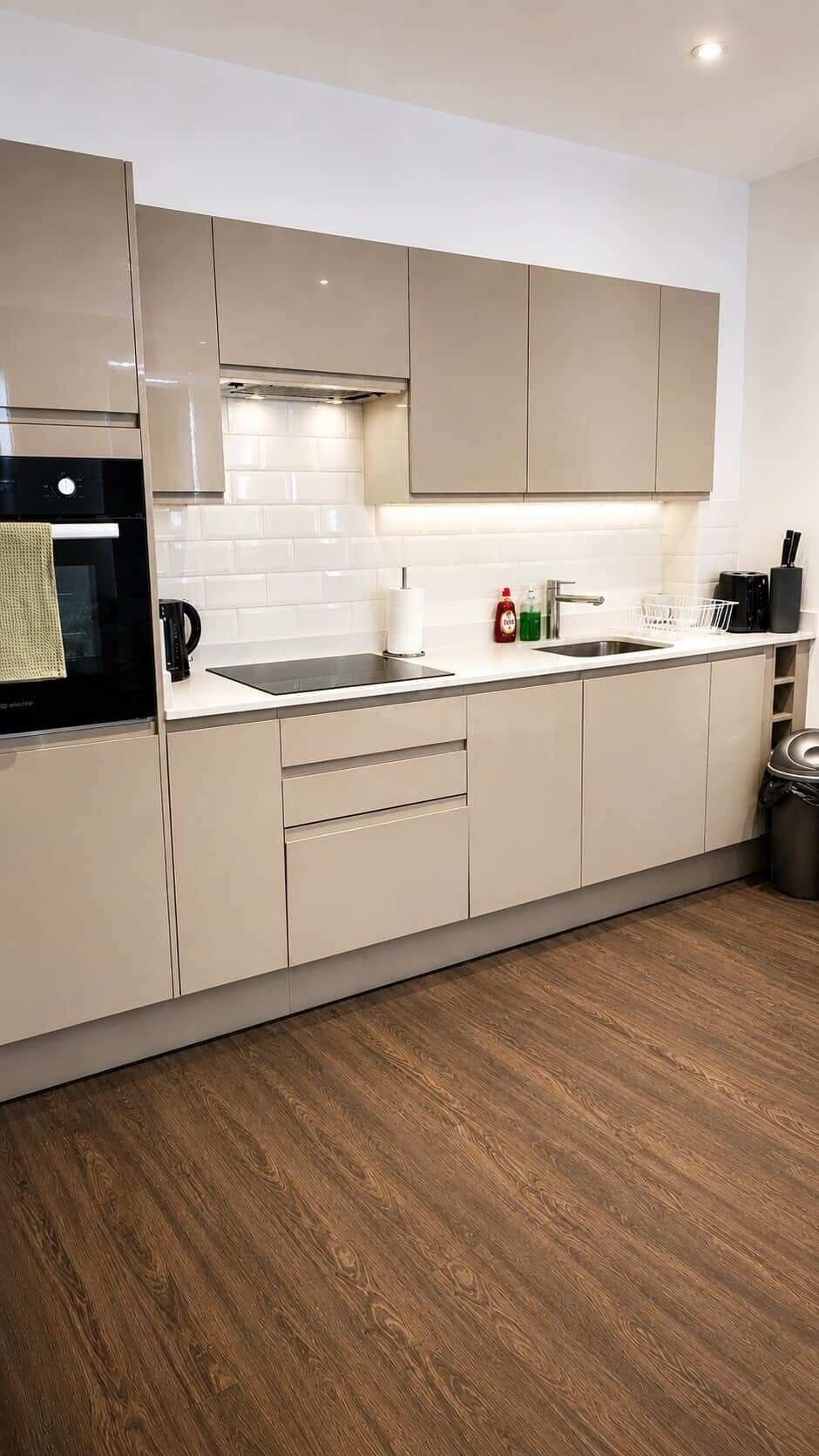 A modern kitchen with a built-in oven, a stainless steel sink, and a wooden floor.