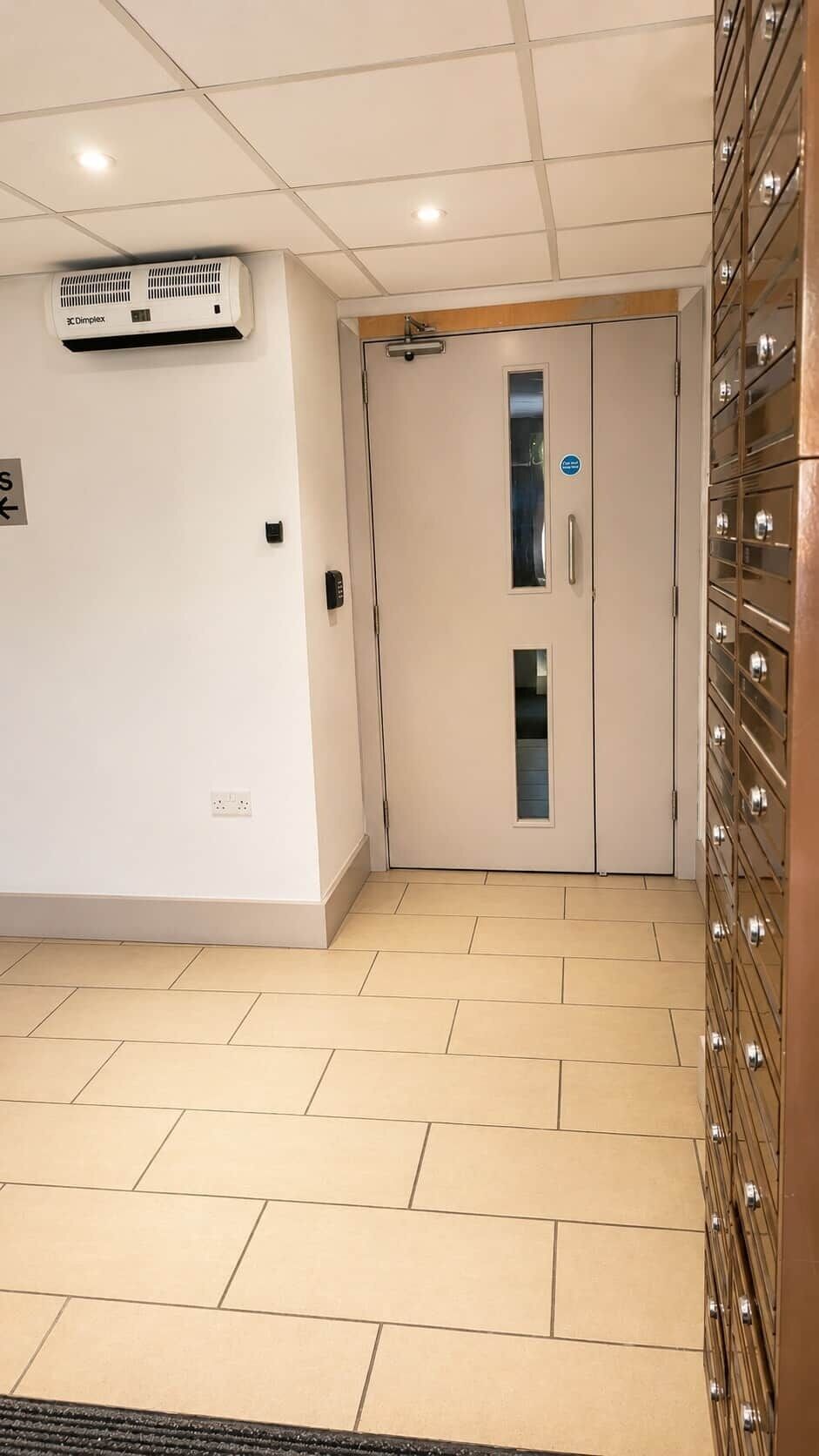 A hallway with a ceiling-mounted air conditioner, a door with a peephole, and a wall-mounted electrical outlet.