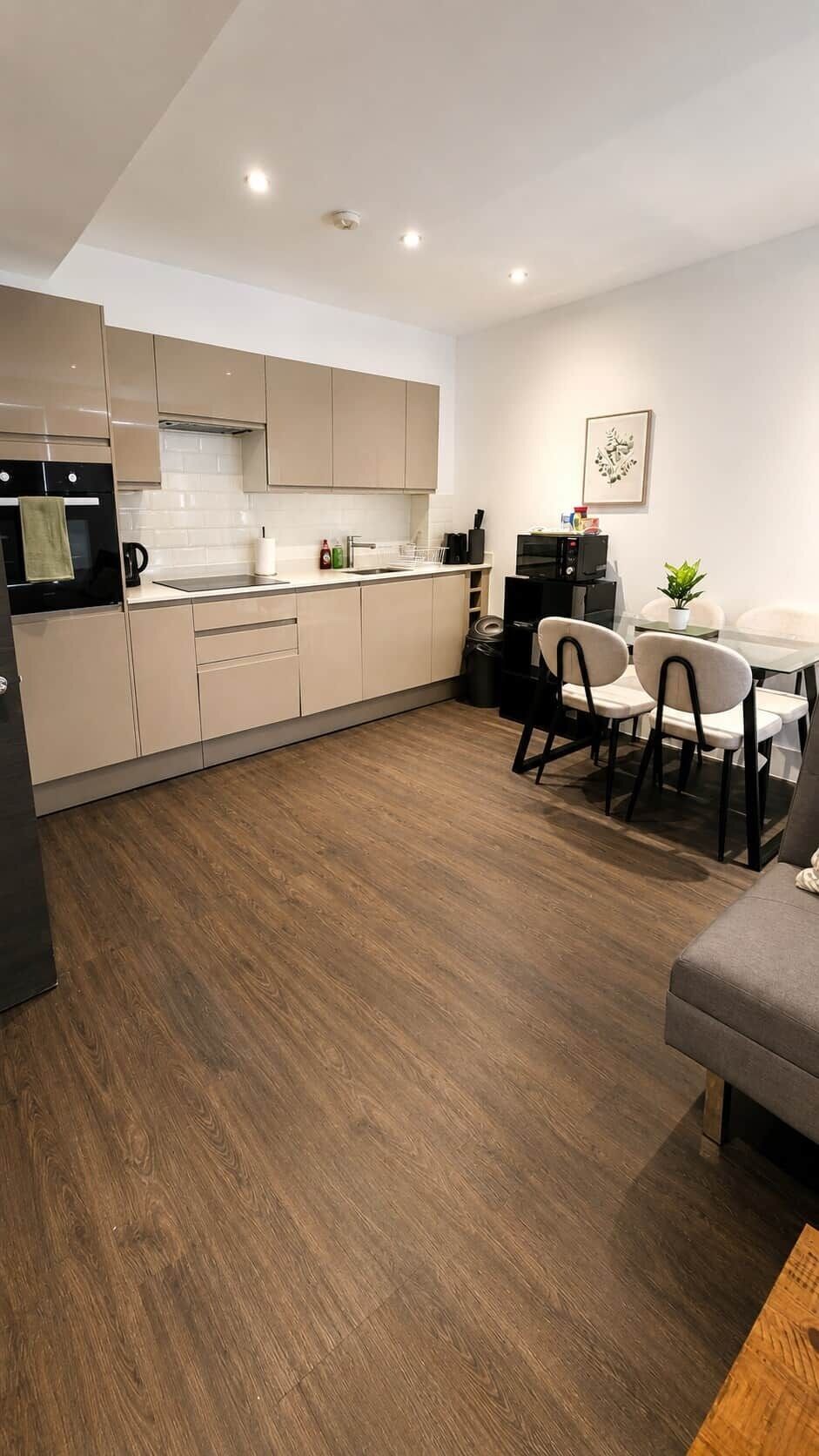 A modern kitchen with a dining area, wooden flooring, and a small table with chairs.