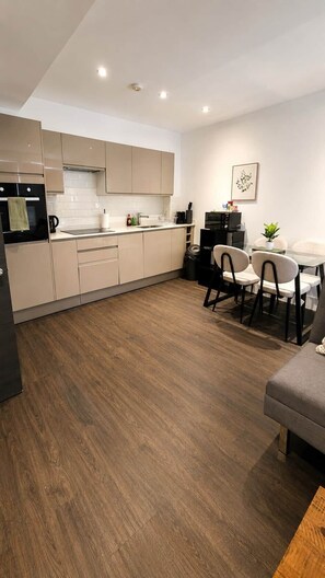 A modern kitchen with a dining area, wooden flooring, and a small table with chairs. - Watford Central 1BR | Sleeps 4 | Near Harry Potter (Watford)