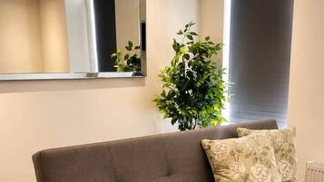 A modern living room with a sofa, a wooden coffee table, a large mirror, and a potted plant.