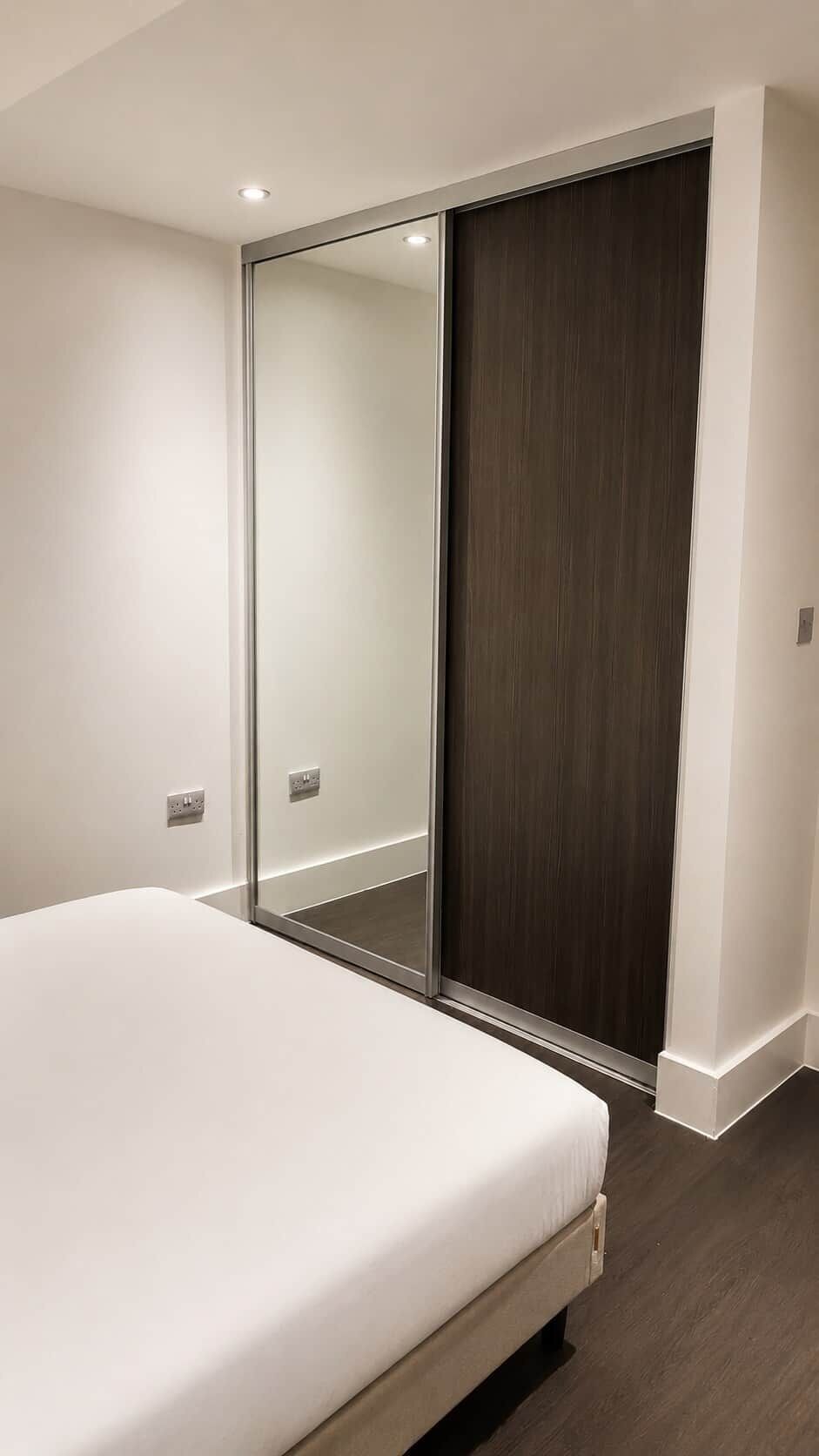 A bedroom with a bed, a dark wooden wardrobe, and a mirrored closet door.