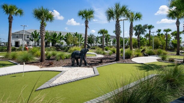 Zona ajardinada con palmeras, una estatua de elefante y un edificio al fondo.