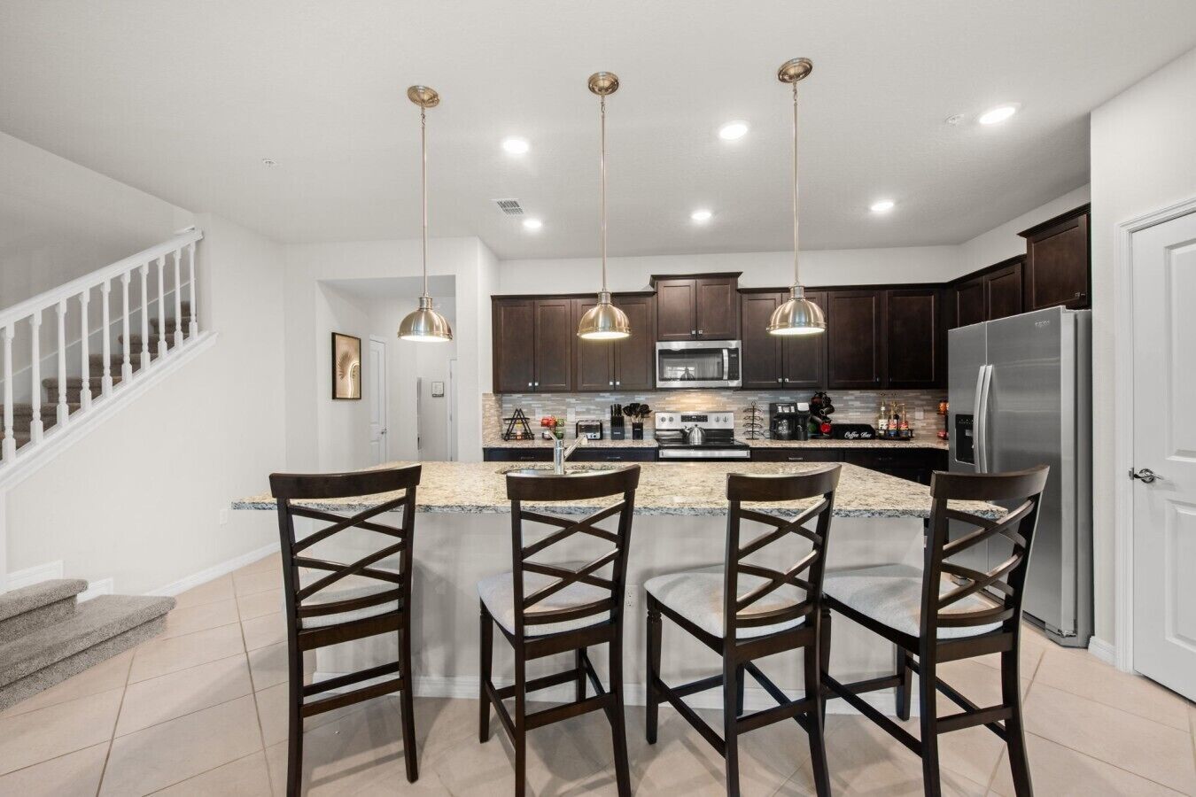 A modern kitchen with a central island, dark wood cabinets, stainless steel appliances, and pendant lighting.