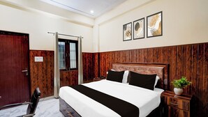Ein Hotelzimmer mit einem hölzernen Kopfteil, einem Bett mit schwarz-weißer Bettwäsche, einem Nachttisch mit Pflanze und einem Fenster mit Gitterstäben.