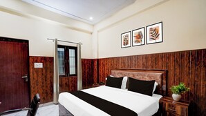 Ein Hotelzimmer mit einem Bett, einem Schreibtisch, einem Stuhl, einem Nachttisch mit Pflanze und einem Fenster mit Gitterstäben.