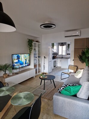 Ein modernes Wohnzimmer mit Fernseher, Sitzecke und einer Küche im Hintergrund.