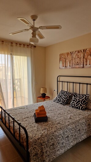 A bedroom with a bed, a ceiling fan, a nightstand with a lamp, and a window with curtains. - Yellowstone (AN)
