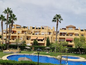 A residential building with multiple balconies, a swimming pool, and palm trees. - Yellowstone (AN)