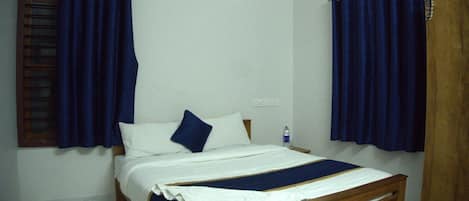 A single bed with a wooden frame, white bedding, and a blue accent pillow.