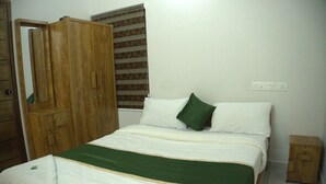A bedroom with a bed, a wooden wardrobe, and a window with blinds. - Pop Tavern Nakshatra Apartments  (Thiruvananthapuram)