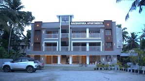 A multi-story building with the name 'NAKSHATRA APARTMENTS' on the facade, featuring balconies, a gated entrance, and a parking area with a car and bicycle. - Pop Tavern Nakshatra Apartments  (Thiruvananthapuram)