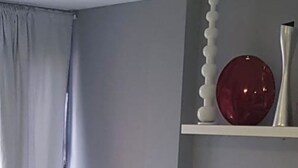 En moderne stue med en grå sofa, en mørk lænestol og en rød dekorativ genstand på en hylde.