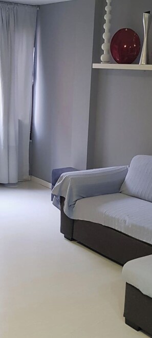 Ein modernes Wohnzimmer mit einem grauen Sofa, einem dunklen Sessel und einem roten Dekorationsobjekt auf einem Regal.