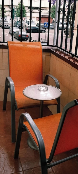Ein kleiner Sitzbereich im Freien mit zwei orangefarbenen Stühlen und einem runden Tisch.