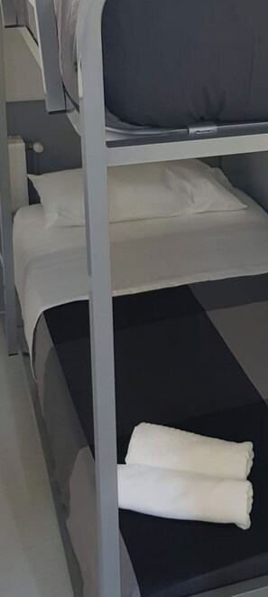 Ein Stockbett mit weißer Bettwäsche und einem gefalteten weißen Handtuch auf der unteren Liege.