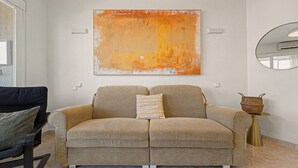 Ein Wohnzimmer mit einem beigefarbenen Sofa, einem großen abstrakten Gemälde, einem runden Spiegel und einem kleinen Beistelltisch.