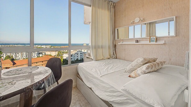 Ein Hotelzimmer mit großem Fenster, einem Bett, einem Nachttisch und einem Sessel.