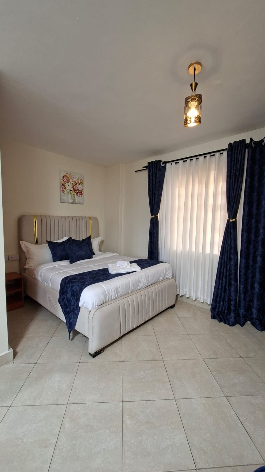 A bedroom with a bed, curtains, a painting, and a ceiling light fixture.