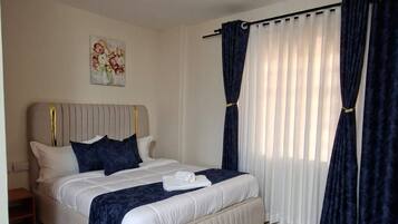 A bedroom with a bed, curtains, a painting, and a ceiling light fixture.