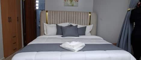 Un dormitorio con una cama grande, cabecera, lámpara de pared y una puerta que da a otra habitación.