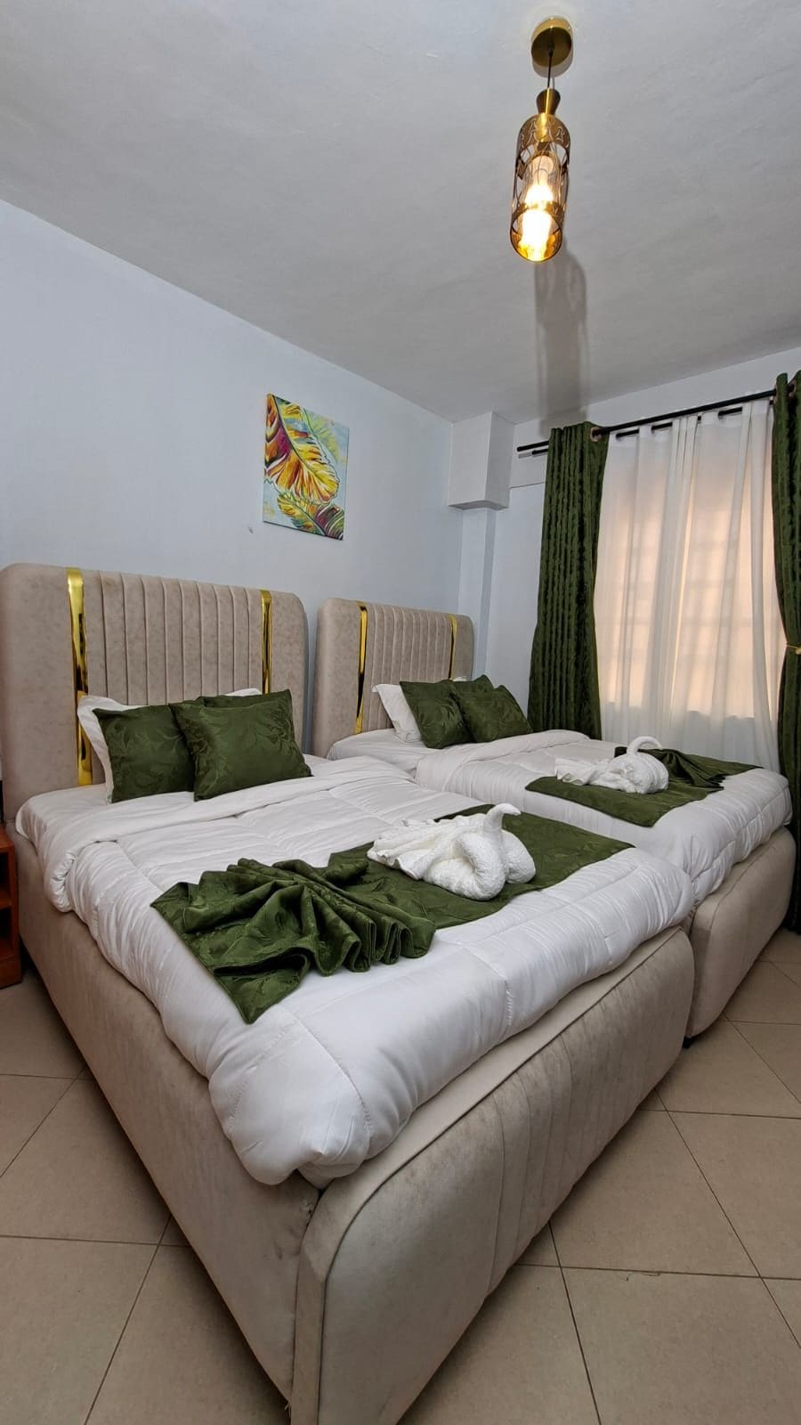 Una cama doble con ropa de cama verde y almohadas blancas, un aplique de techo y un cuadro en la pared.