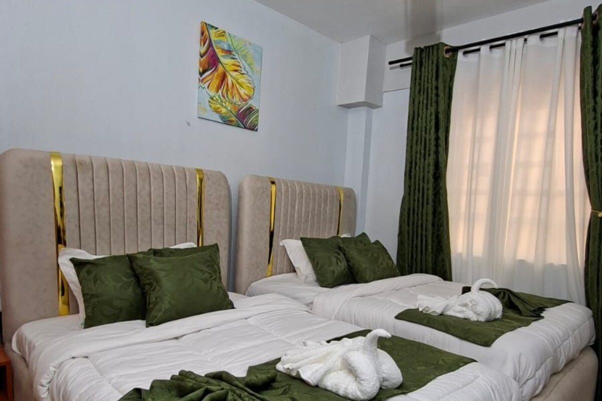 A double bed with green bedding and white pillows, a ceiling light fixture, and a painting on the wall.