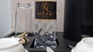 A minibar setup with a bottle labeled 'NOVARA HOTEL,' a glass, a coffee maker, and white cups and saucers. - Novara Hotel Mwihoko  (Nairobi)