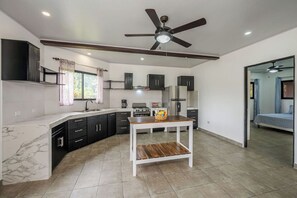 A modern kitchen with dark cabinets, a white countertop, and a ceiling fan. - Buena Vista Escape | Lake Views, Pool & Nature (Tilarán)