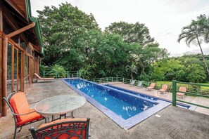 Una piscina exterior amb gandules i una taula, envoltada de vegetació exuberanta.