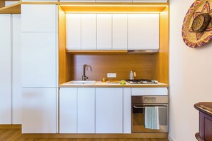 Une cuisine compacte dotée de meubles blancs, d’un évier en acier inoxydable, d’une cuisinière à gaz et d’un lave-vaisselle.